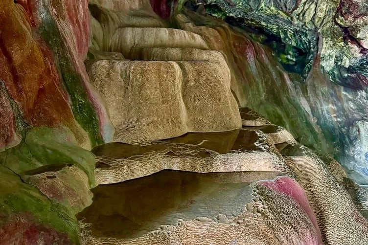 The cave has become a landmark as a natural spring drips from the roof, creating colourful red, blue, and white mineral deposits and stepped limestone pools (Picture: Holywell Bay Surf Life Saving Club)